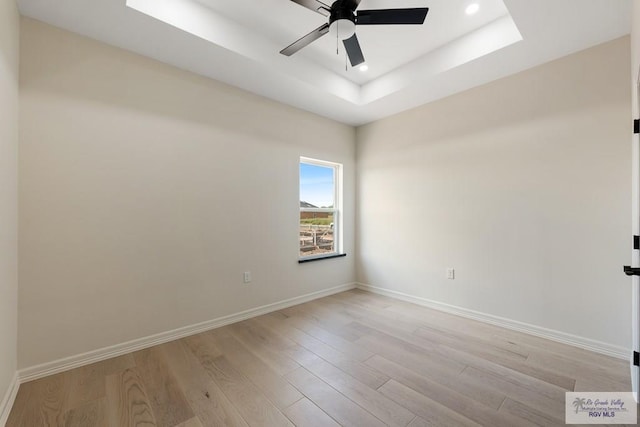 spare room featuring a raised ceiling, light hardwood / wood-style flooring, and ceiling fan