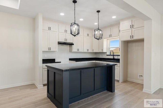 1209 Bridle Way, San Benito, TX 78586 - kitchen with under cabinet range hood, dark countertops, light wood-type flooring, a center island, and recessed lighting