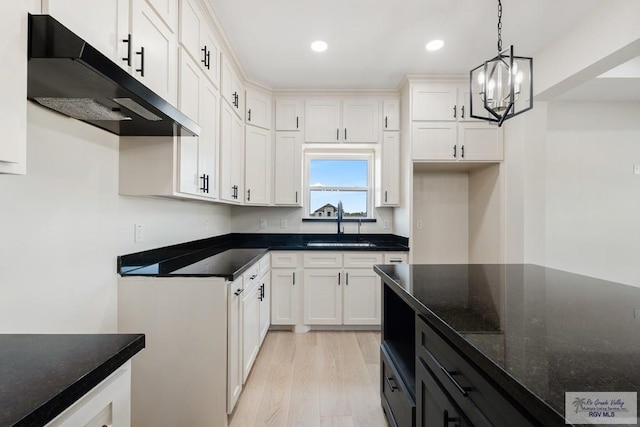 kitchen with pendant lighting, dark stone counters, light wood-type flooring, a notable chandelier, and white cabinetry