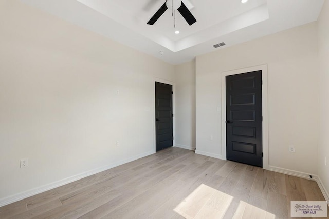 unfurnished room featuring ceiling fan, light hardwood / wood-style floors, and a tray ceiling