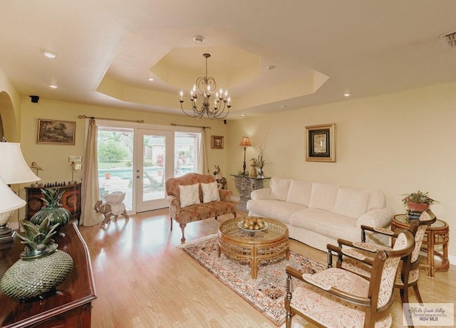 living room featuring french doors, light wood-type flooring, a tray ceiling, and a notable chandelier