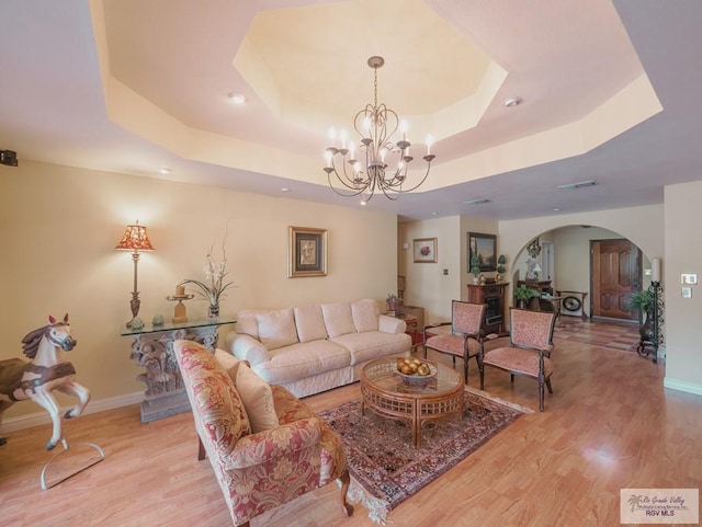 living room with a tray ceiling, a chandelier, and light wood-type flooring