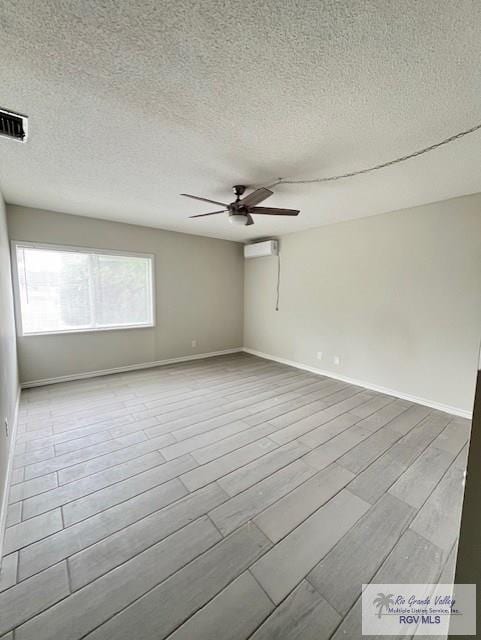 empty room featuring ceiling fan, light wood-type flooring, a textured ceiling, and an AC wall unit