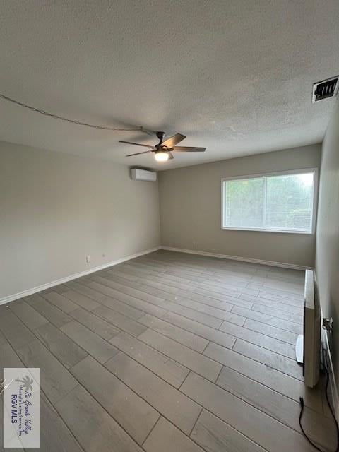 empty room with ceiling fan, light hardwood / wood-style floors, a textured ceiling, and a wall unit AC