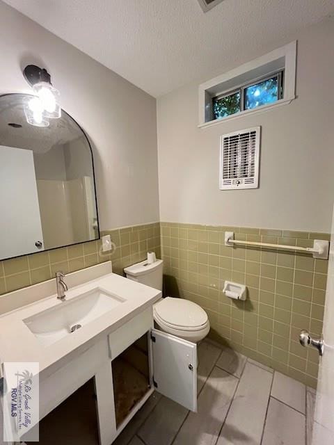 bathroom with tile patterned floors, a textured ceiling, toilet, vanity, and tile walls