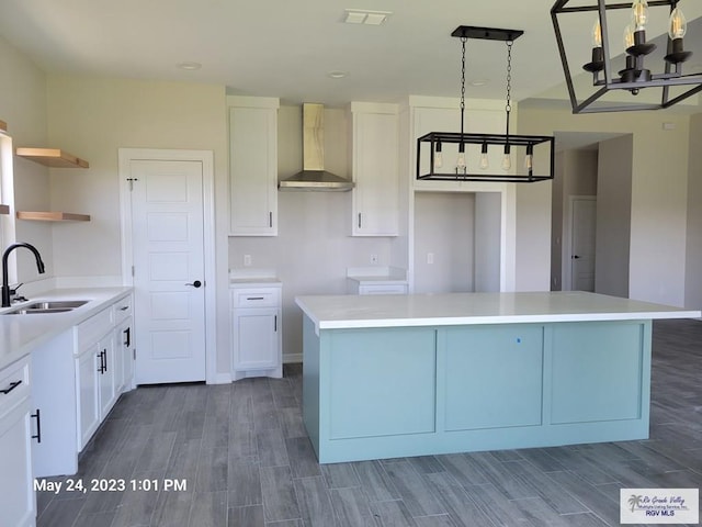 kitchen with an inviting chandelier, wood finished floors, a center island, wall chimney exhaust hood, and a sink