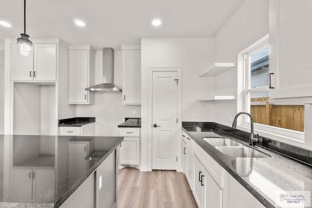 kitchen with wall chimney range hood, open shelves, a sink, white cabinets, and dark stone counters