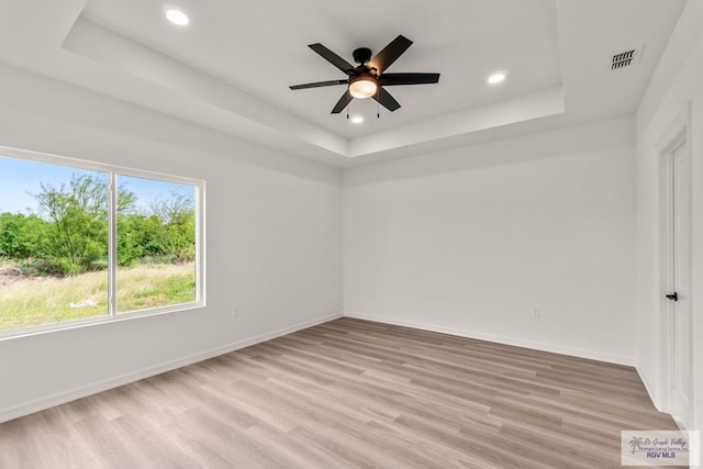 empty room featuring ceiling fan, visible vents, light wood-type flooring, a tray ceiling, and recessed lighting