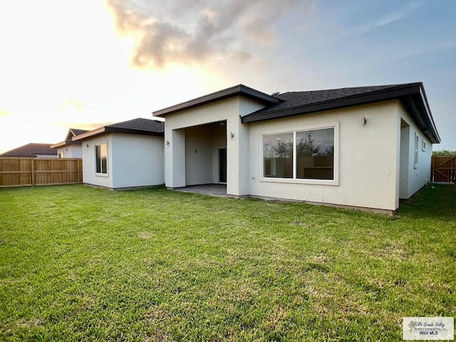 back of property with fence, stucco siding, a lawn, and a shingled roof