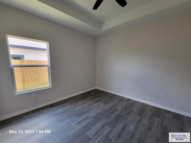 unfurnished room featuring baseboards, a ceiling fan, a raised ceiling, and dark wood-style floors