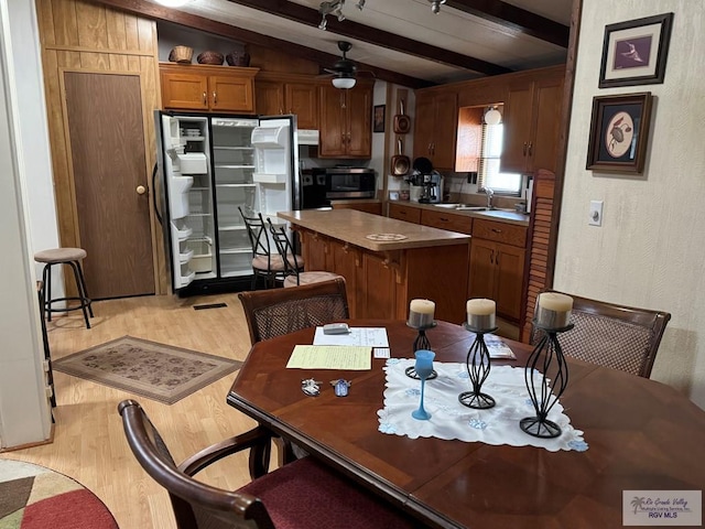 kitchen with sink, vaulted ceiling with beams, fridge, a kitchen island, and light wood-type flooring