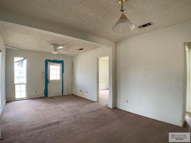 carpeted spare room with a textured ceiling, baseboards, visible vents, and ceiling fan