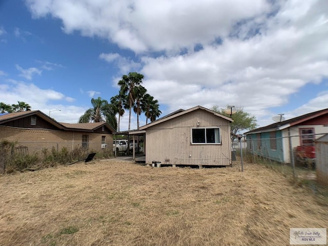 rear view of property featuring a carport, an outbuilding, a yard, and fence