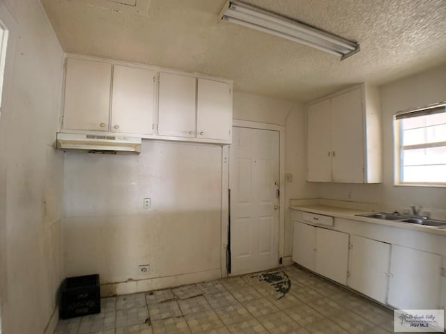 kitchen featuring under cabinet range hood, white cabinets, light countertops, and a sink