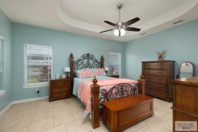 tiled bedroom with ceiling fan and a tray ceiling