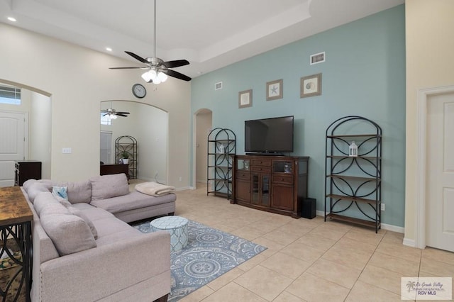 living room with light tile patterned floors, ceiling fan, a high ceiling, and a tray ceiling