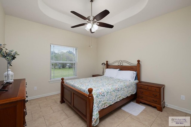 tiled bedroom with ceiling fan and a tray ceiling