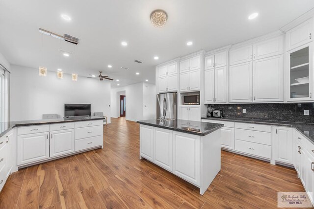 kitchen featuring light wood-type flooring, tasteful backsplash, stainless steel appliances, ceiling fan, and white cabinets