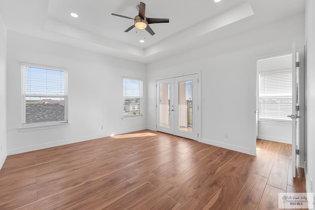 spare room featuring hardwood / wood-style flooring, ceiling fan, a tray ceiling, and french doors