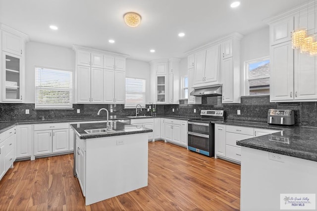 kitchen featuring extractor fan, stainless steel electric range oven, light hardwood / wood-style floors, white cabinetry, and an island with sink