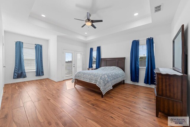 bedroom with wood-type flooring, access to outside, a raised ceiling, and ceiling fan