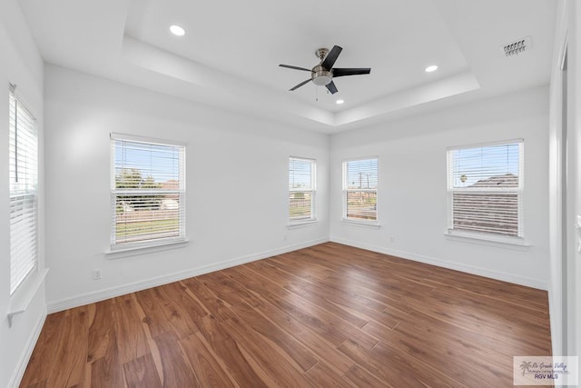 empty room with hardwood / wood-style flooring, ceiling fan, and a tray ceiling