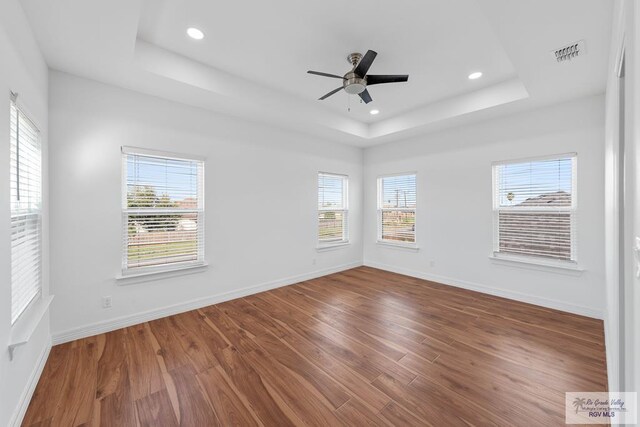 empty room with hardwood / wood-style flooring, ceiling fan, and a tray ceiling