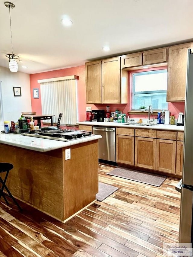 kitchen with sink, decorative light fixtures, light hardwood / wood-style flooring, appliances with stainless steel finishes, and kitchen peninsula