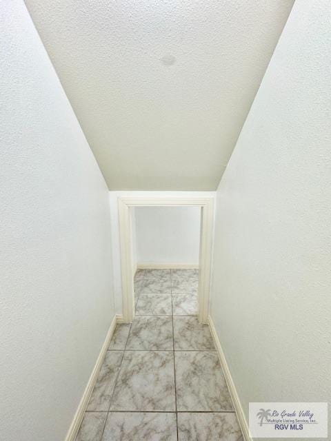 hallway with light tile patterned floors, a textured ceiling, and vaulted ceiling