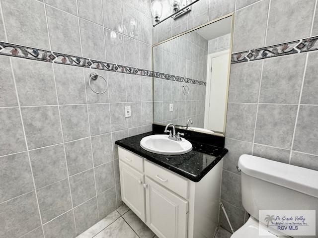 bathroom with tile patterned floors, vanity, tile walls, and toilet