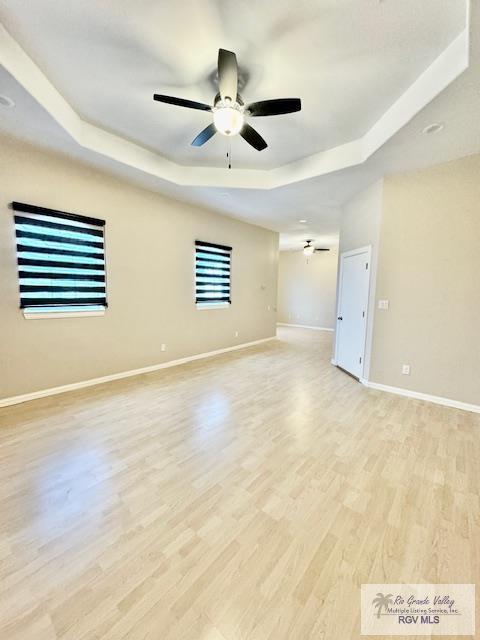 unfurnished room featuring light hardwood / wood-style floors, ceiling fan, and a tray ceiling