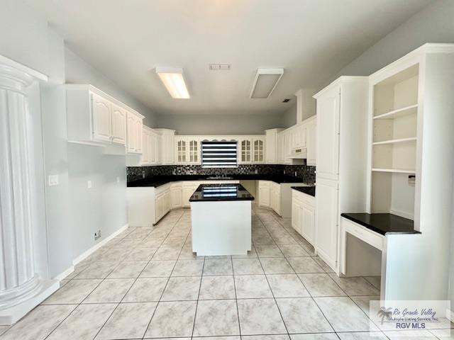 kitchen with ornate columns, a kitchen island, light tile patterned flooring, ventilation hood, and white cabinets