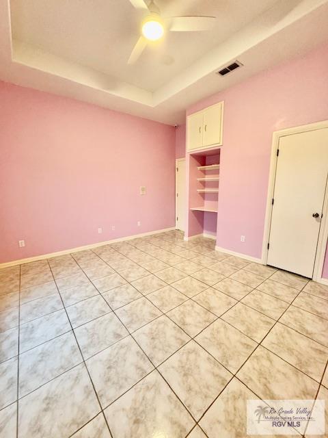 unfurnished bedroom featuring a walk in closet, a closet, a raised ceiling, and ceiling fan