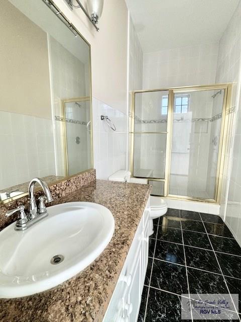 bathroom with walk in shower, vanity, toilet, and tile walls