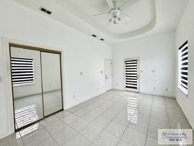 unfurnished bedroom with a tray ceiling, ceiling fan, a closet, and light tile patterned flooring