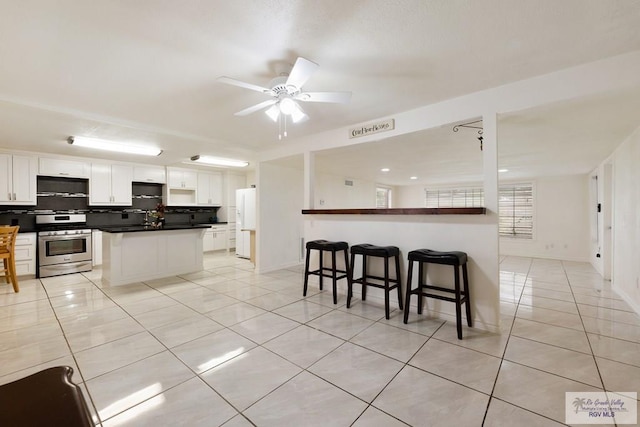 kitchen with backsplash, stainless steel range, ceiling fan, exhaust hood, and white cabinetry