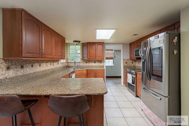 kitchen featuring sink, light tile patterned floors, appliances with stainless steel finishes, kitchen peninsula, and a breakfast bar area