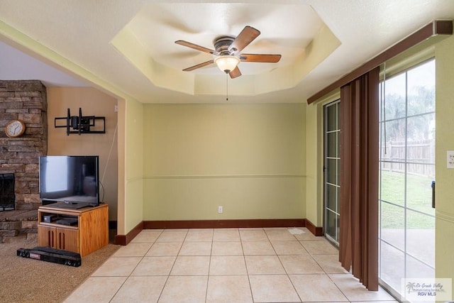 unfurnished living room with light tile patterned floors, a tray ceiling, and ceiling fan