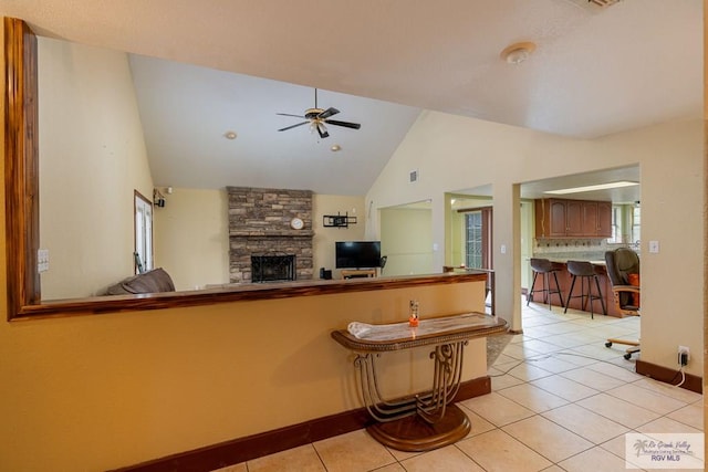 kitchen with ceiling fan, a fireplace, light tile patterned floors, and high vaulted ceiling