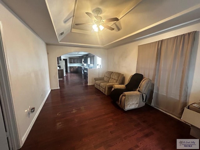 living room featuring a raised ceiling, ceiling fan, and dark wood-type flooring