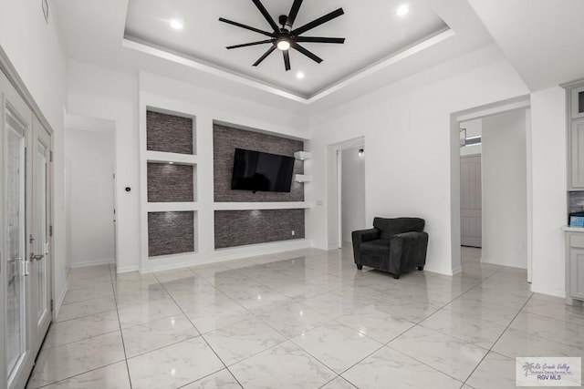 unfurnished living room with a tray ceiling, a ceiling fan, french doors, and marble finish floor