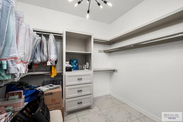 spacious closet with built in study area, marble finish floor, and a chandelier