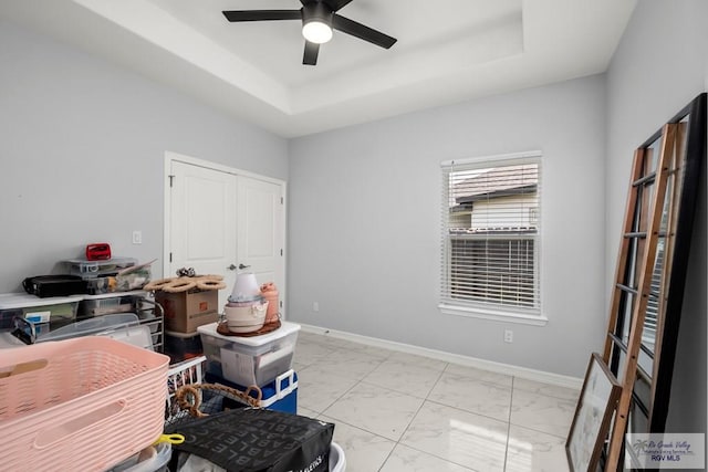 interior space with baseboards, marble finish floor, ceiling fan, and a tray ceiling