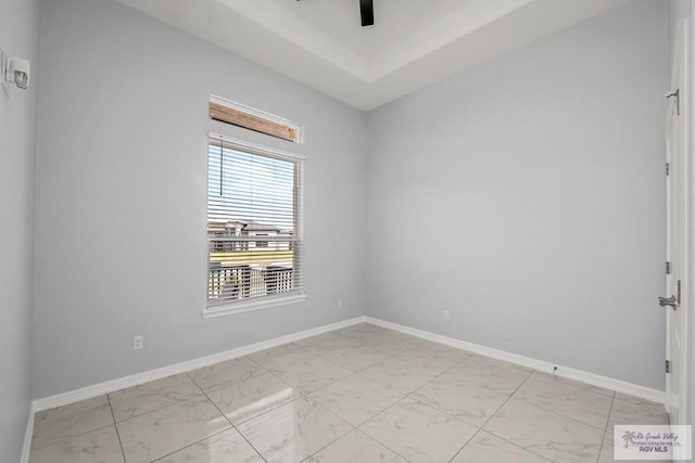 empty room featuring baseboards, a ceiling fan, a raised ceiling, and marble finish floor