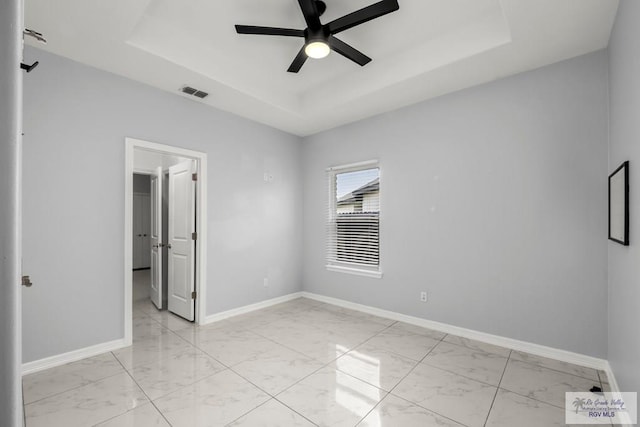 unfurnished bedroom featuring visible vents, marble finish floor, baseboards, a walk in closet, and a tray ceiling