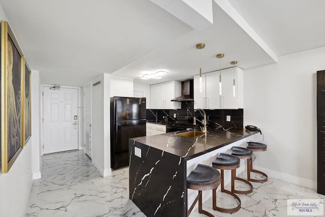 kitchen featuring marble finish floor, wall chimney range hood, a peninsula, and freestanding refrigerator