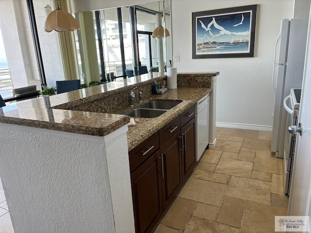 kitchen with dark stone counters, dark brown cabinetry, white dishwasher, sink, and an island with sink