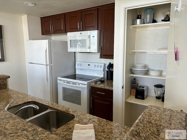 kitchen featuring dark stone countertops, dark brown cabinetry, sink, and white appliances