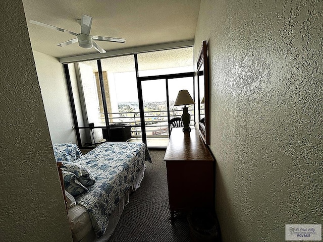 bedroom with a wall of windows, ceiling fan, and dark colored carpet