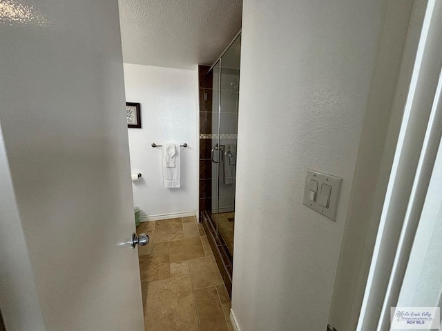 bathroom featuring a textured ceiling, baseboards, a stall shower, and stone finish flooring
